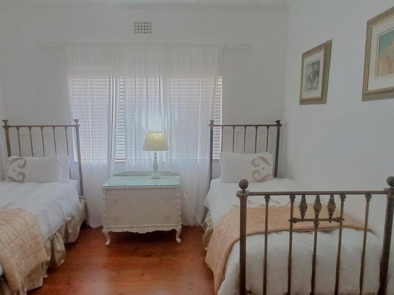 A bedroom featuring hardwood flooring and a central ventilation grille, illuminated by natural light through window coverings.