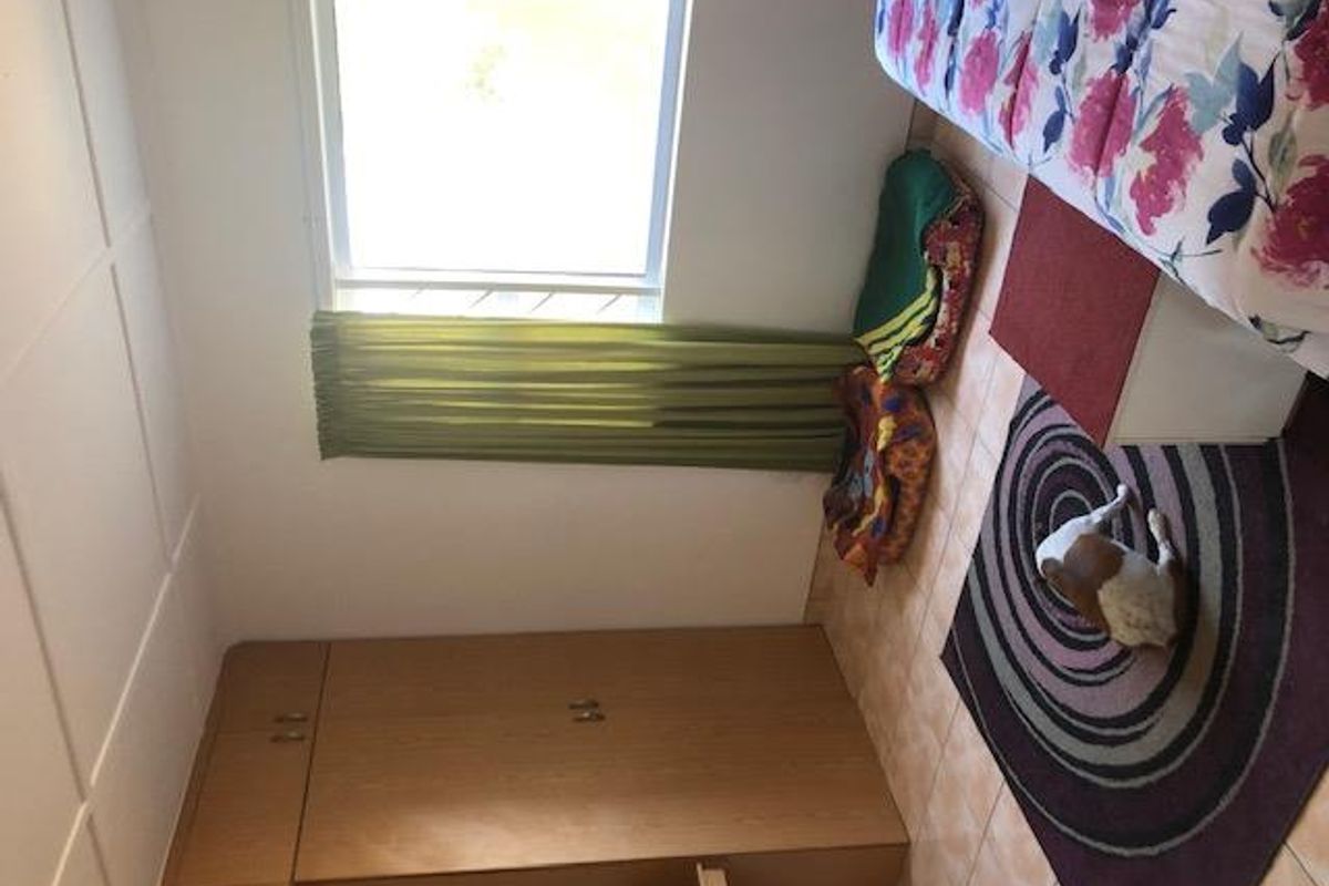 A bedroom featuring built-in wooden cupboards, tiled flooring, and a window with curtains.