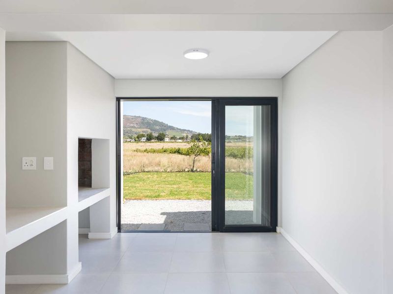 A bright, modern covered patio featuring a built-in braai, tiled flooring, and large sliding glass doors opening to a scenic garden view.