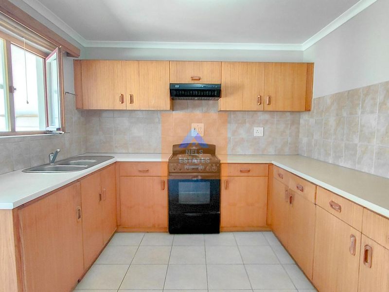A functional kitchen featuring wooden cabinetry, a double bowl sink, and a freestanding oven with an extractor fan, finished with tiled splashbacks.
