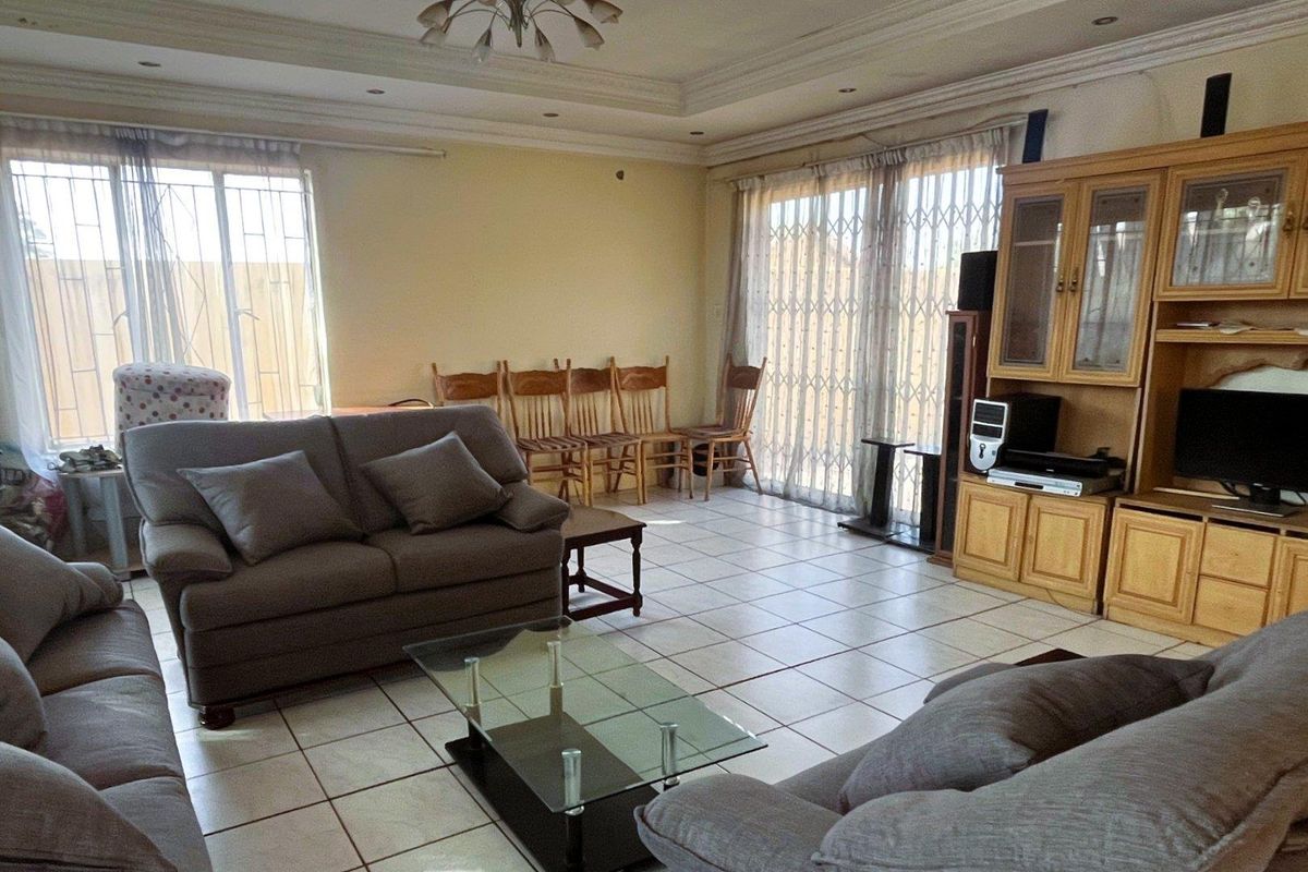 Spacious living room featuring tiled flooring, recessed ceiling detail, and large sliding glass doors with security gates providing access to the exterior.