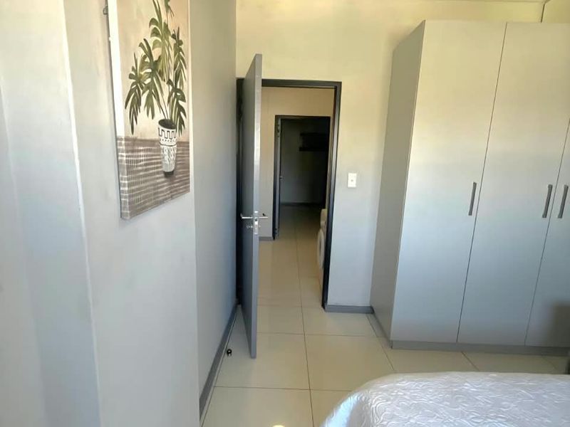 A bedroom featuring neutral tiled flooring and a built-in wardrobe, with a doorway leading to an adjacent room.