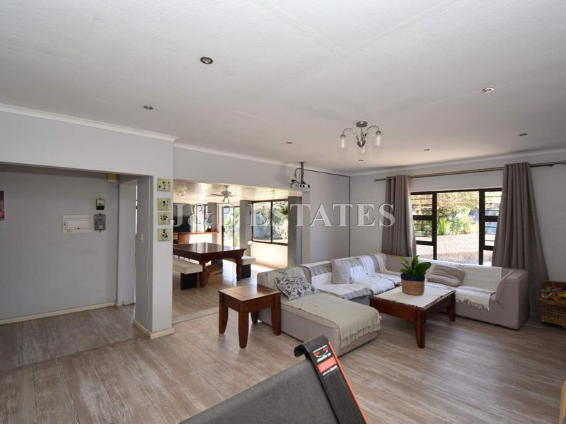 Spacious open-plan living area featuring light wood-look flooring, recessed ceiling lighting, and large windows providing natural light and garden views.