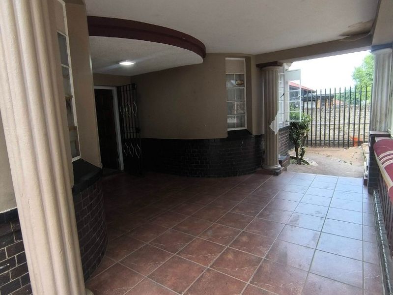 A covered patio area featuring tiled flooring, decorative columns, and a recessed ceiling, providing a sheltered outdoor space.