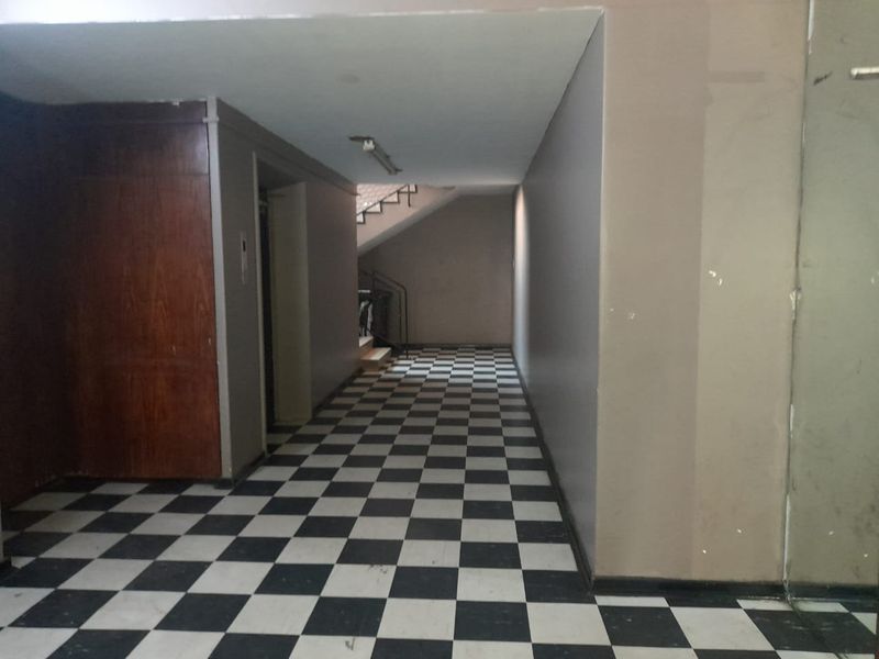 A vacant apartment building hallway featuring checkered tile flooring, wood paneling, an elevator access point, and a staircase leading to upper levels.
