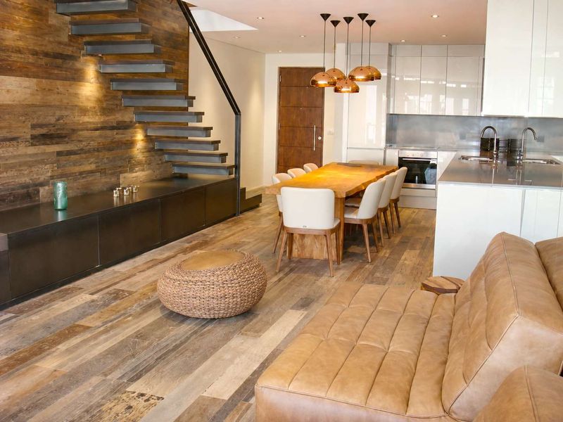 Modern open-plan living area featuring a striking floating staircase, wood-paneled feature wall, and a sleek, contemporary kitchen with integrated appliances.