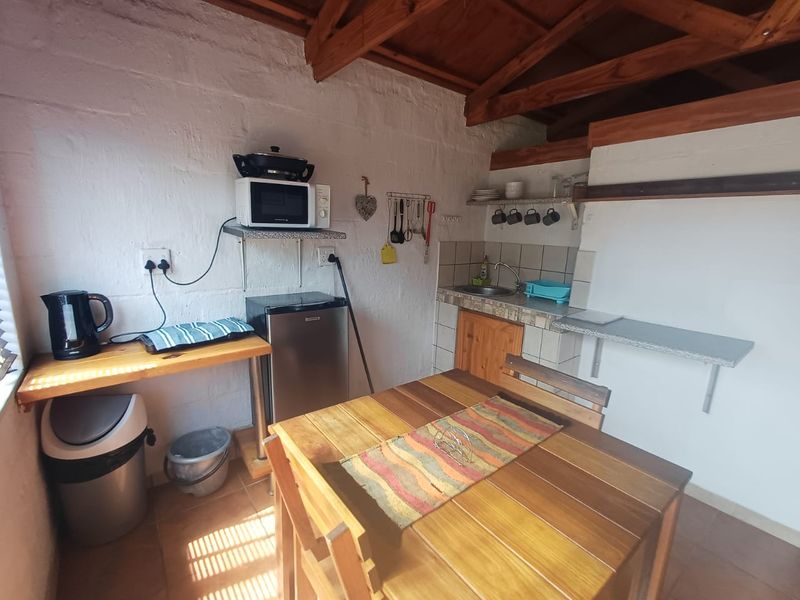 A rustic kitchenette featuring exposed timber roof trusses, tiled splashback, stainless steel sink, and built-in shelving with tiled flooring.