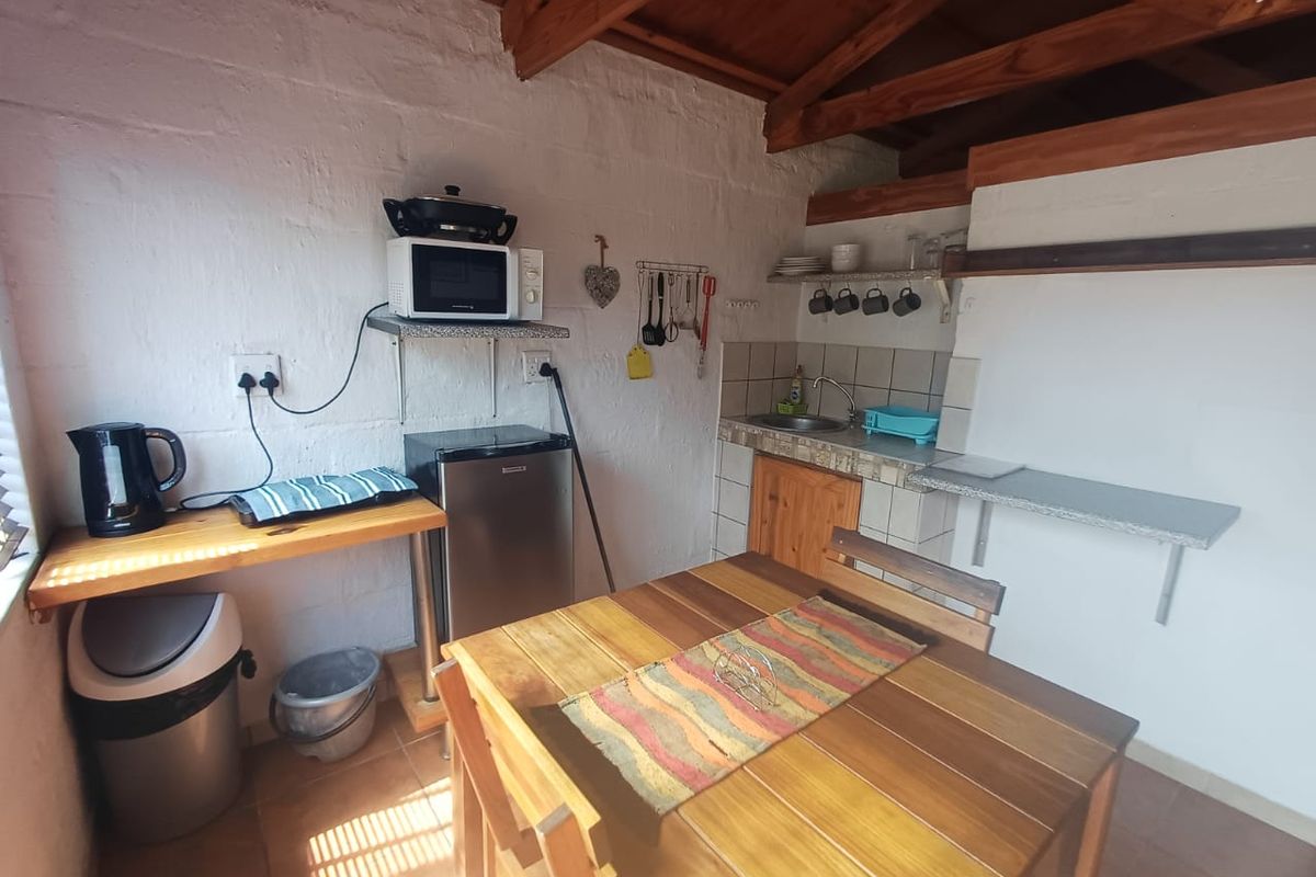 A rustic kitchenette featuring exposed timber roof trusses, tiled splashback, stainless steel sink, and built-in shelving with tiled flooring.