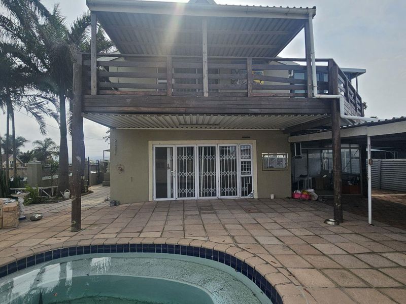 Rear exterior view featuring a paved patio area, swimming pool, and a raised wooden deck with a covered structure.