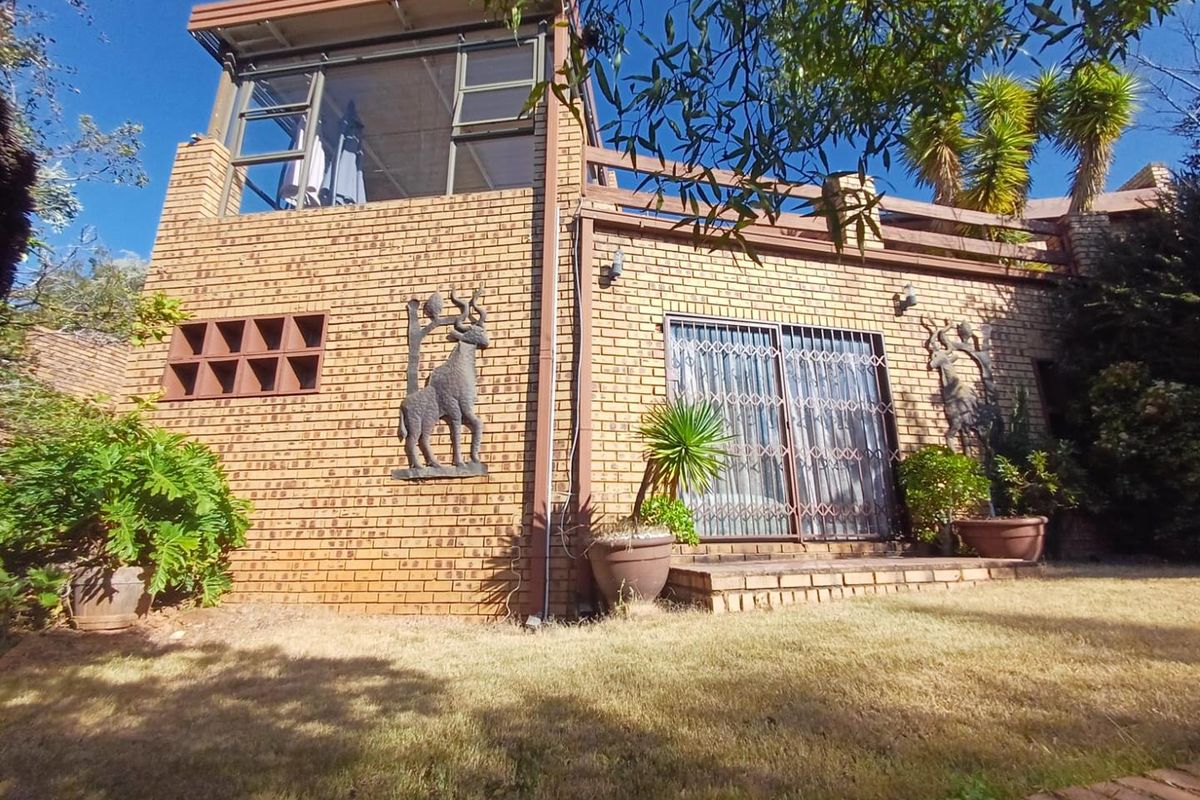 Rear view of a double-story brick house featuring a balcony, sliding glass doors with security gates, and a landscaped garden area.
