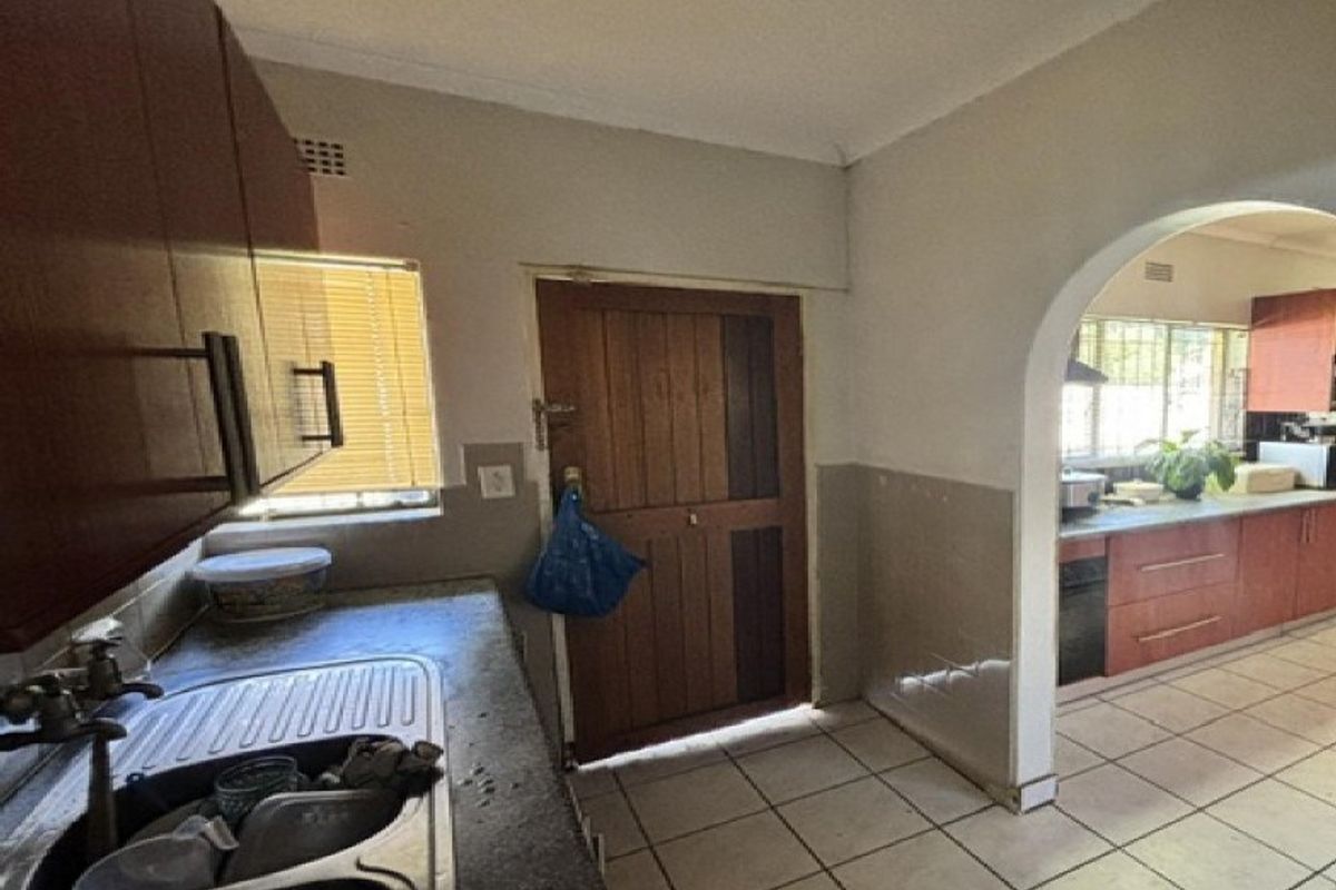 A dated kitchen featuring built-in cabinetry, tiled flooring, and an arched entryway connecting to an adjacent prep area with a built-in oven.