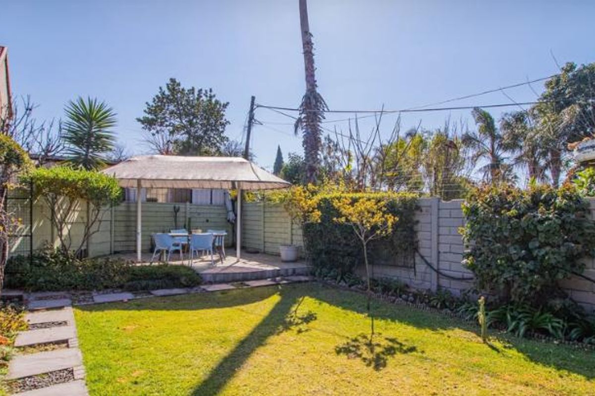 A private rear garden featuring a paved patio area with a shade canopy, established landscaping, and perimeter walling.