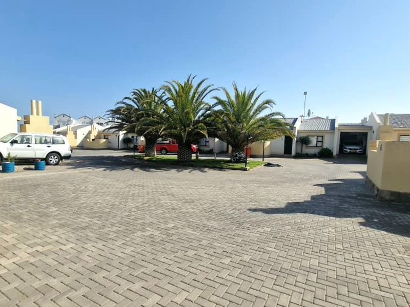 A wide-angle view of the townhouse complex entrance featuring paved driveways, established palm trees, and multiple garage access points.
