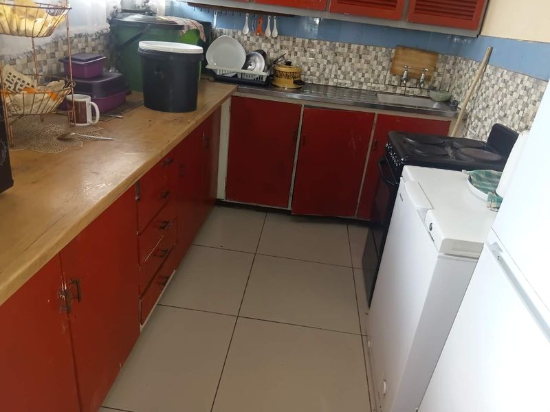 A functional kitchen featuring red cabinetry, tiled backsplash, stainless steel sink, and tiled flooring, offering potential for modernization and cosmetic updates.