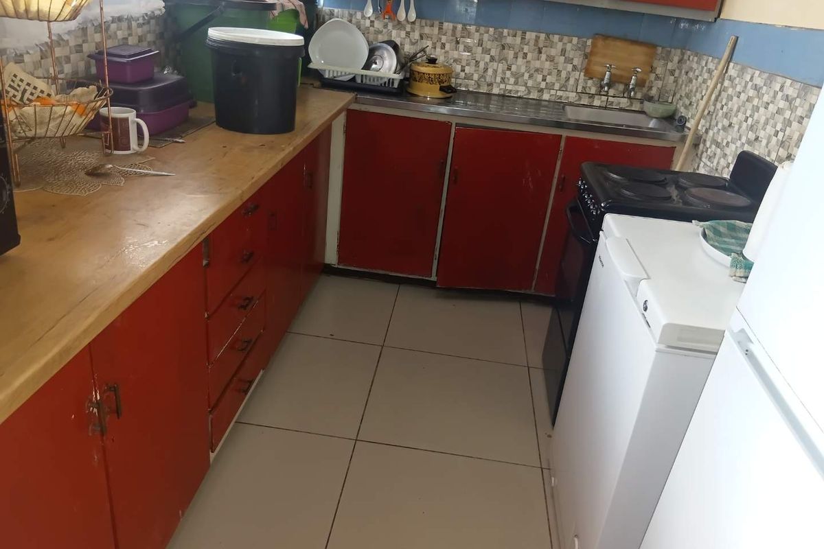 A functional kitchen featuring red cabinetry, tiled backsplash, stainless steel sink, and tiled flooring, offering potential for modernization and cosmetic updates.
