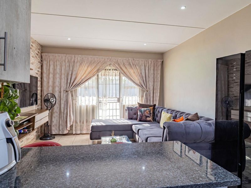 Open-plan living area featuring a granite kitchen countertop, stone feature wall, and tiled flooring, seamlessly connecting to a bright lounge space.