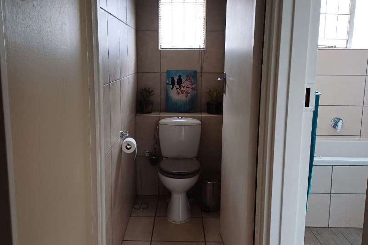 A functional bathroom featuring tiled walls and flooring, a standard toilet, and a view into the adjacent bathing area.