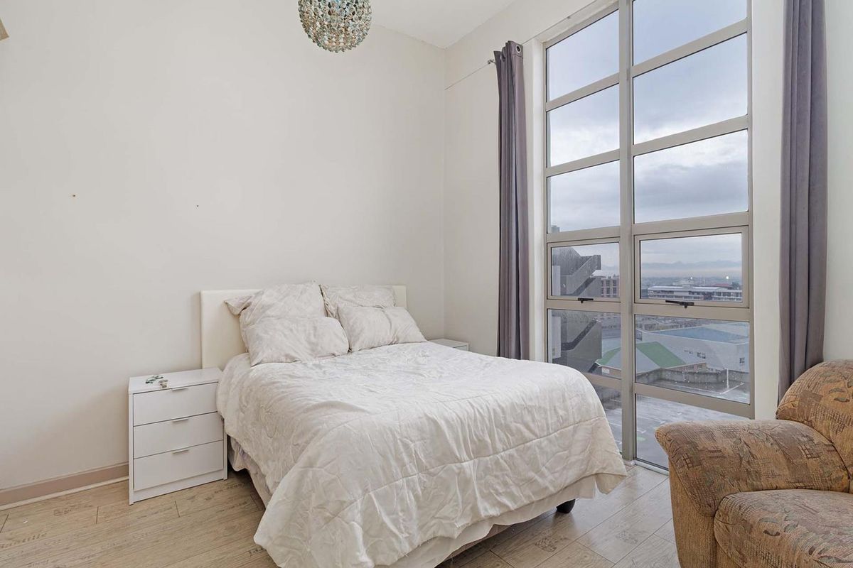 A bright bedroom featuring floor-to-ceiling windows that provide ample natural light and an urban view.