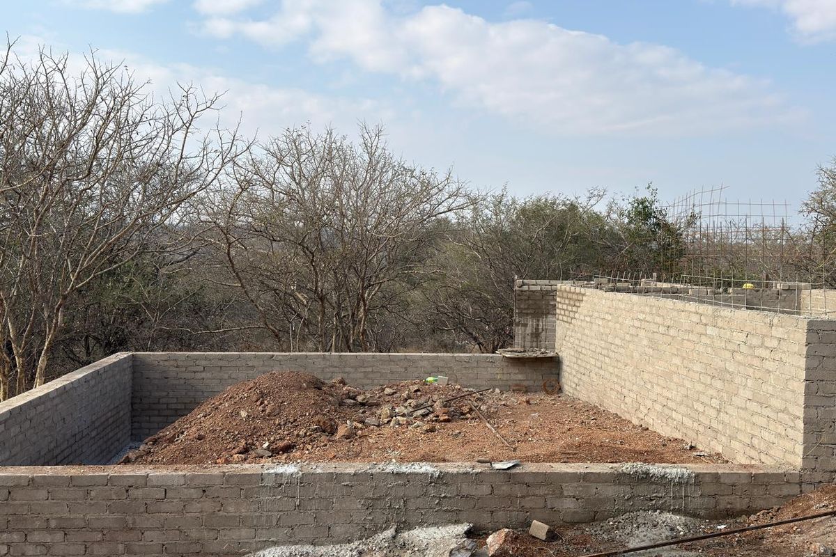 An unfinished construction site showing exposed concrete block walls and foundation work in a rural setting.
