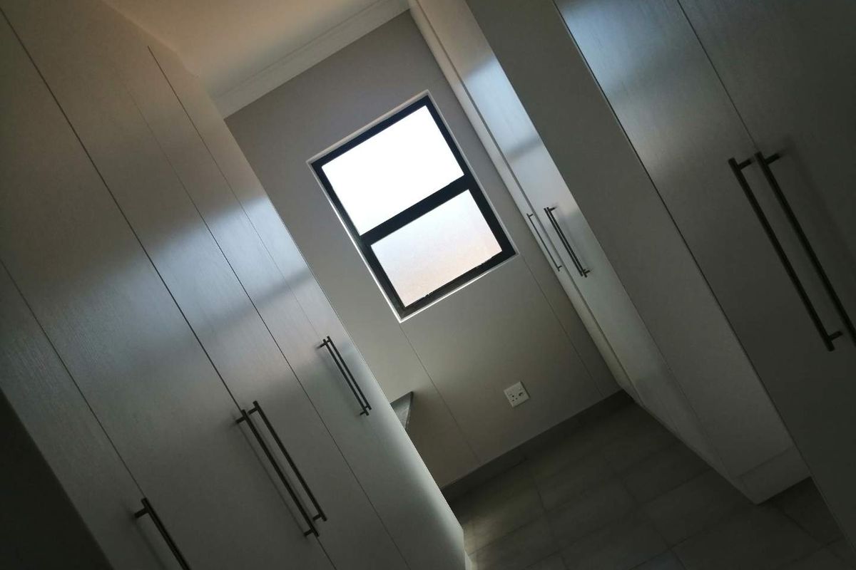 A clean, modern walk-in closet or dressing area featuring extensive built-in cabinetry, tiled flooring, and a neutral color palette.
