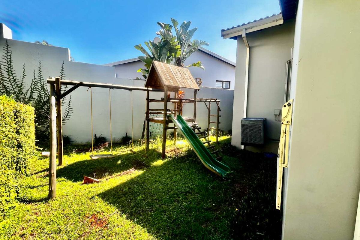 A private rear garden area featuring a lawn and a fixed wooden children's play structure with a slide.