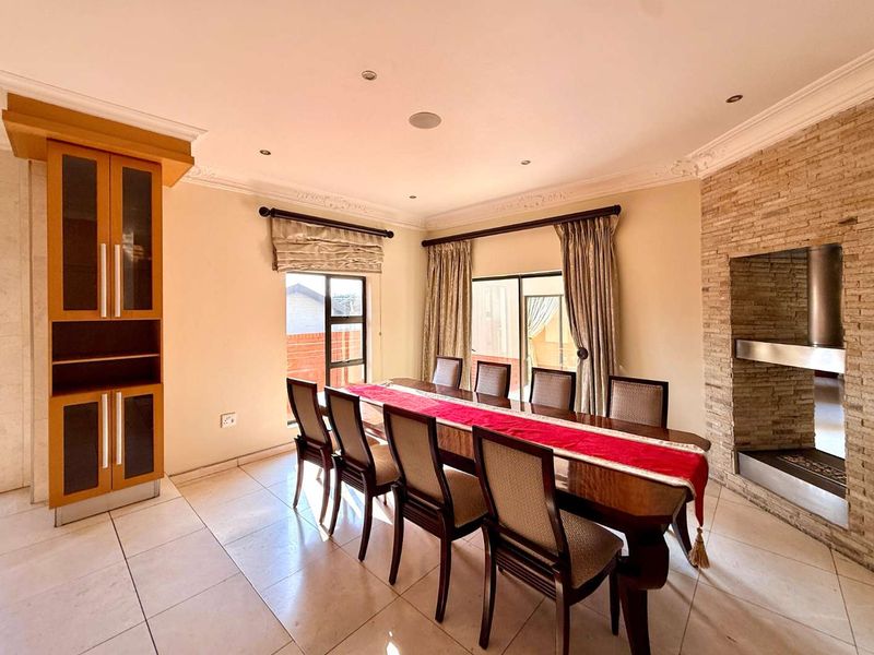 Spacious dining room featuring tiled flooring, a stone-clad fireplace, built-in cabinetry, and decorative ceiling cornices, creating an elegant space for formal meals.