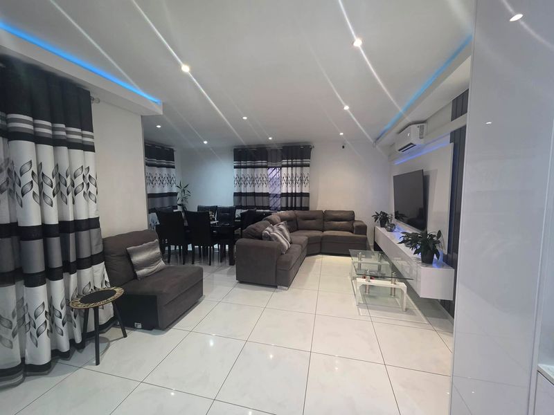 A modern open-plan living and dining area featuring polished tiled flooring, recessed ceiling lighting with LED accents, and a sleek built-in media console.