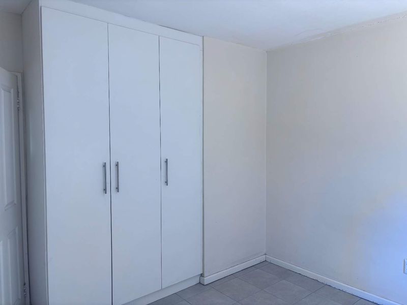 A simple, empty bedroom featuring white built-in wardrobes, tiled flooring, and neutral wall finishes.