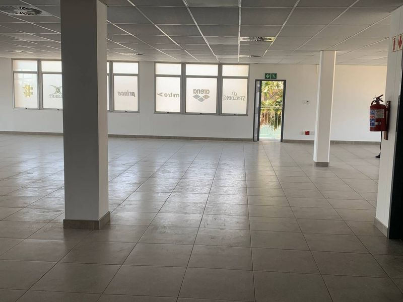 Spacious open-plan industrial office area featuring tiled flooring, suspended ceilings, structural columns, and direct access to an outdoor balcony.