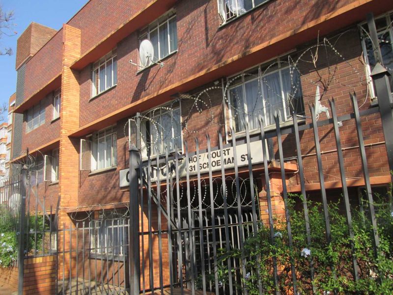 Front exterior view of a multi-story brick apartment building featuring security fencing and razor wire perimeter protection.