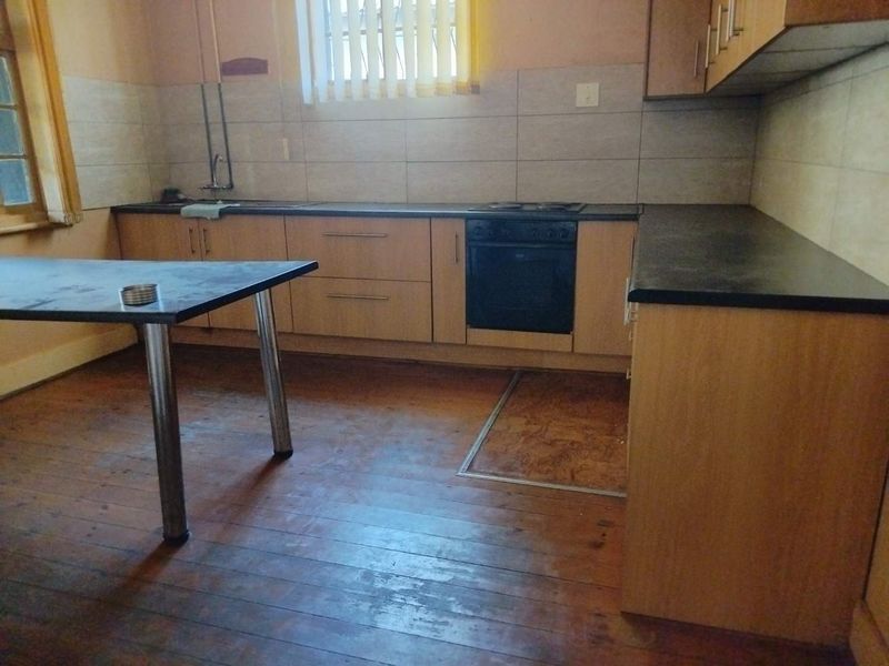 A dated kitchen featuring timber flooring, laminate countertops, built-in cabinetry, and integrated oven and hob, requiring cosmetic updates to improve its overall condition.