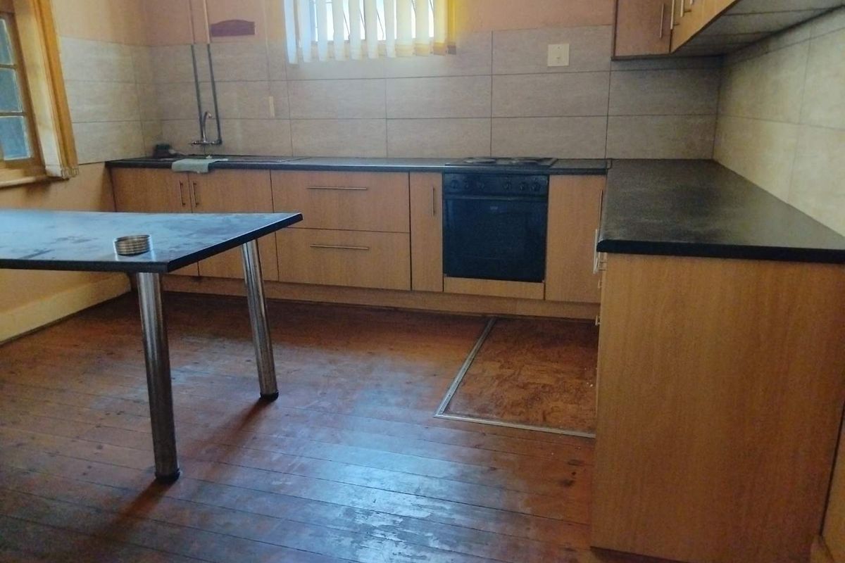 A dated kitchen featuring timber flooring, laminate countertops, built-in cabinetry, and integrated oven and hob, requiring cosmetic updates to improve its overall condition.