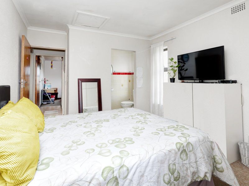 A bedroom featuring an en-suite bathroom, neutral wall finishes, and coving, providing a functional living space with potential for cosmetic updates.