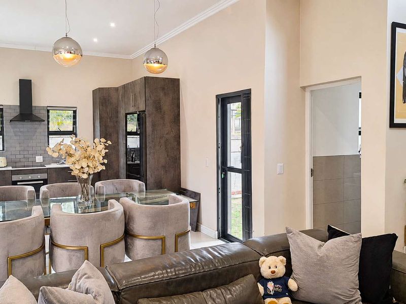 Modern open-plan living and kitchen area featuring contemporary dark cabinetry, subway tile backsplash, and integrated appliances with stylish pendant lighting.