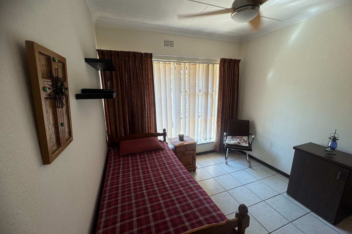 A functional bedroom featuring tiled flooring, a ceiling fan, and vertical blinds, offering a simple and practical living space.