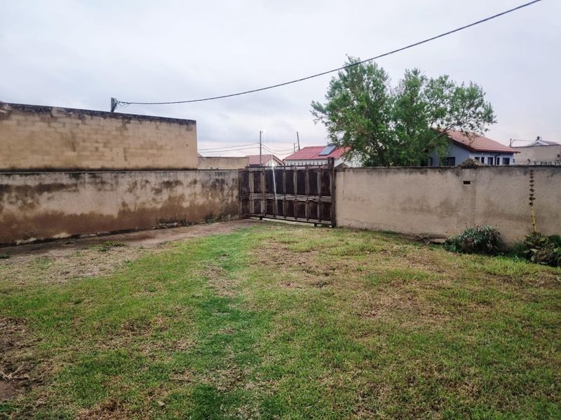 A private backyard area featuring a lawn, perimeter boundary walls, and a metal gate providing access to the property.