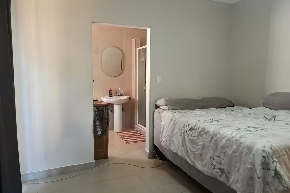 A bedroom featuring neutral walls and tiled flooring, with an adjoining en-suite bathroom equipped with a pedestal sink and a shower enclosure.