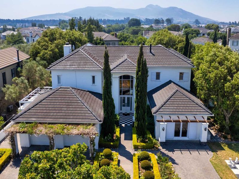 Aerial view of a well-maintained two-story residence featuring a tiled roof, paved driveway, double garage, and landscaped garden in a scenic estate setting.