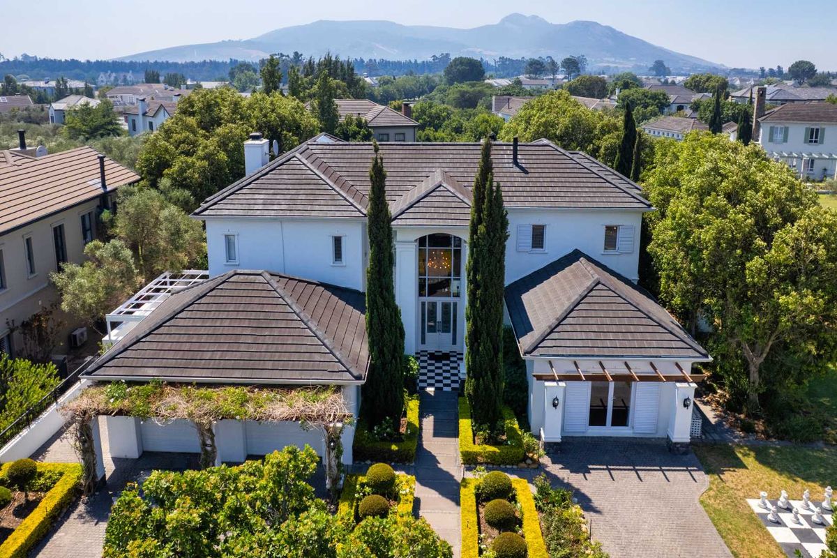 Aerial view of a well-maintained two-story residence featuring a tiled roof, paved driveway, double garage, and landscaped garden in a scenic estate setting.