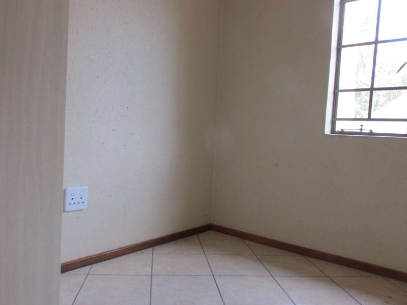 An empty bedroom featuring tiled flooring, neutral walls, and a window with security bars, providing a blank canvas for personalization.
