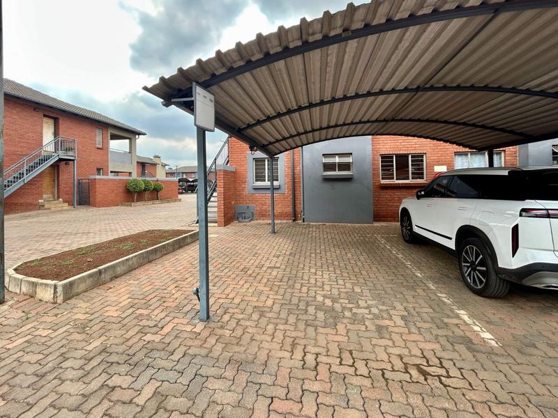 Exterior view of an apartment complex featuring a covered carport, paved driveway, and brick building facade with external staircases.