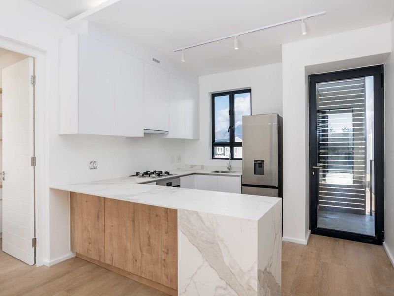 Modern kitchen featuring white and wood-grain cabinetry, stone countertops, integrated gas hob, and a convenient walk-in pantry with direct access to the balcony.