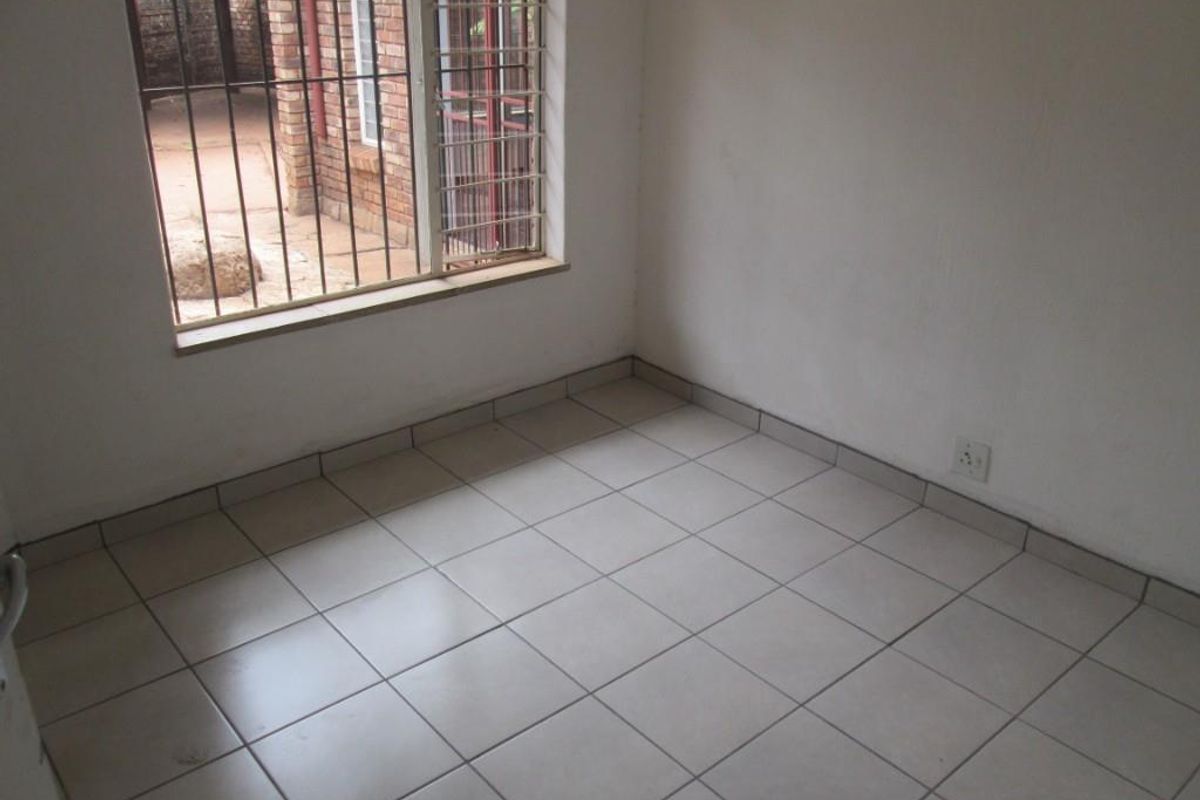 An empty bedroom featuring neutral ceramic floor tiles, white walls, and a window fitted with security bars.
