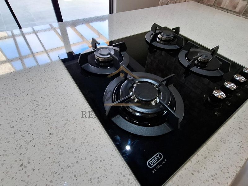 Close-up view of a modern black glass gas hob integrated into a speckled stone countertop with exposed brick detailing in the background.