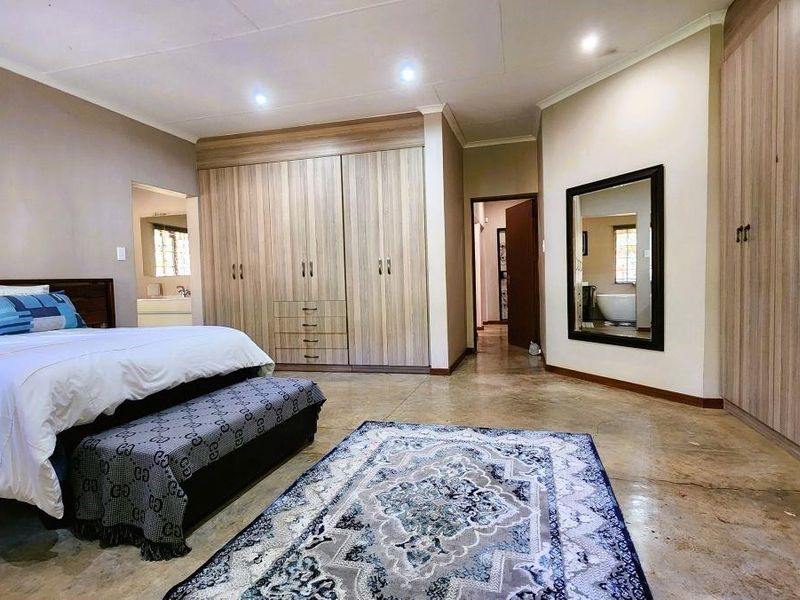 Spacious bedroom featuring extensive built-in wooden cabinetry, polished concrete floors, recessed lighting, and direct access to an en-suite bathroom.