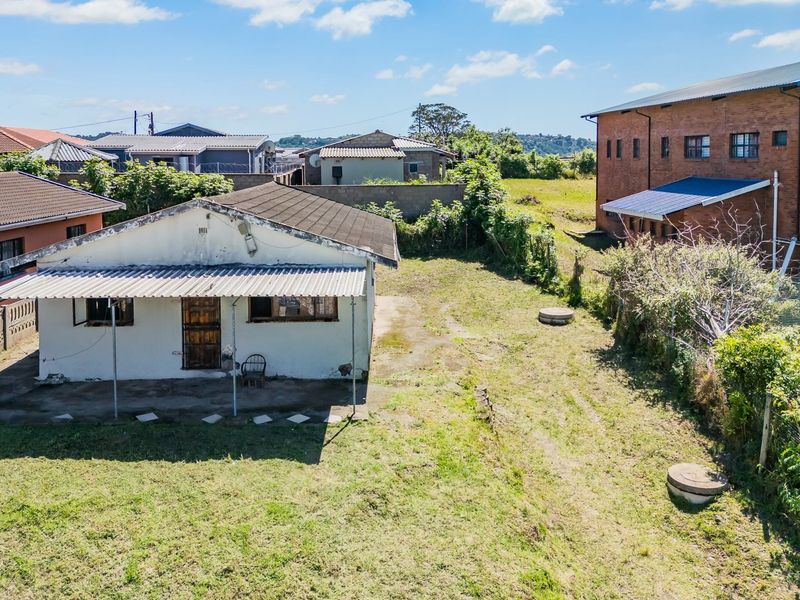 Aerial view of a residential property featuring a detached dwelling with a covered patio, set within a large, partially landscaped yard.
