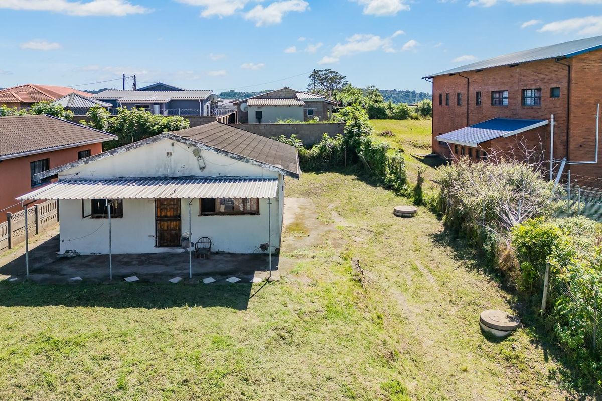 Aerial view of a residential property featuring a detached dwelling with a covered patio, set within a large, partially landscaped yard.