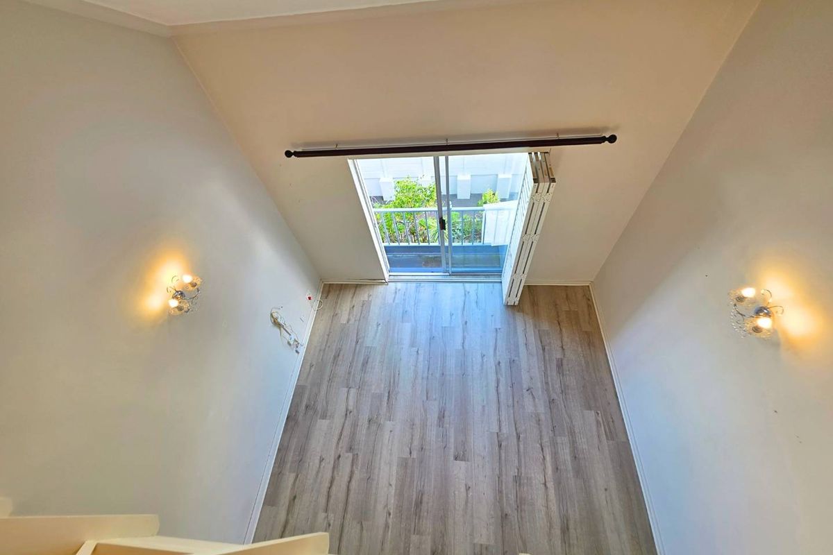 An empty living room with high ceilings, laminate flooring, and a sliding glass door leading to a balcony, viewed from an elevated mezzanine level.