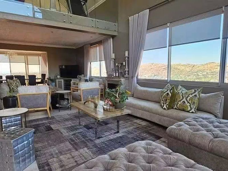 Spacious open-plan living area featuring high ceilings, a glass mezzanine balustrade, large windows with panoramic views, and a fireplace.