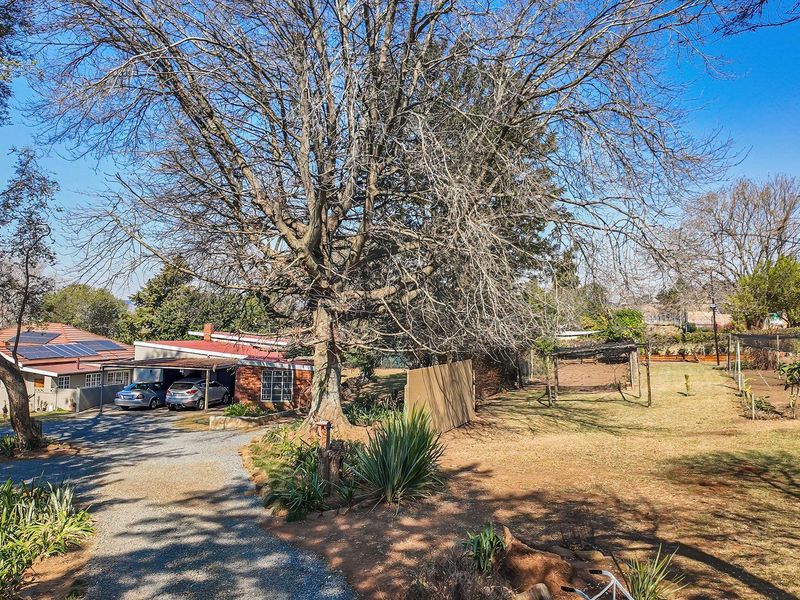 A wide-angle view of the property exterior featuring a gravel driveway, carport, and solar panels set within a spacious garden area.